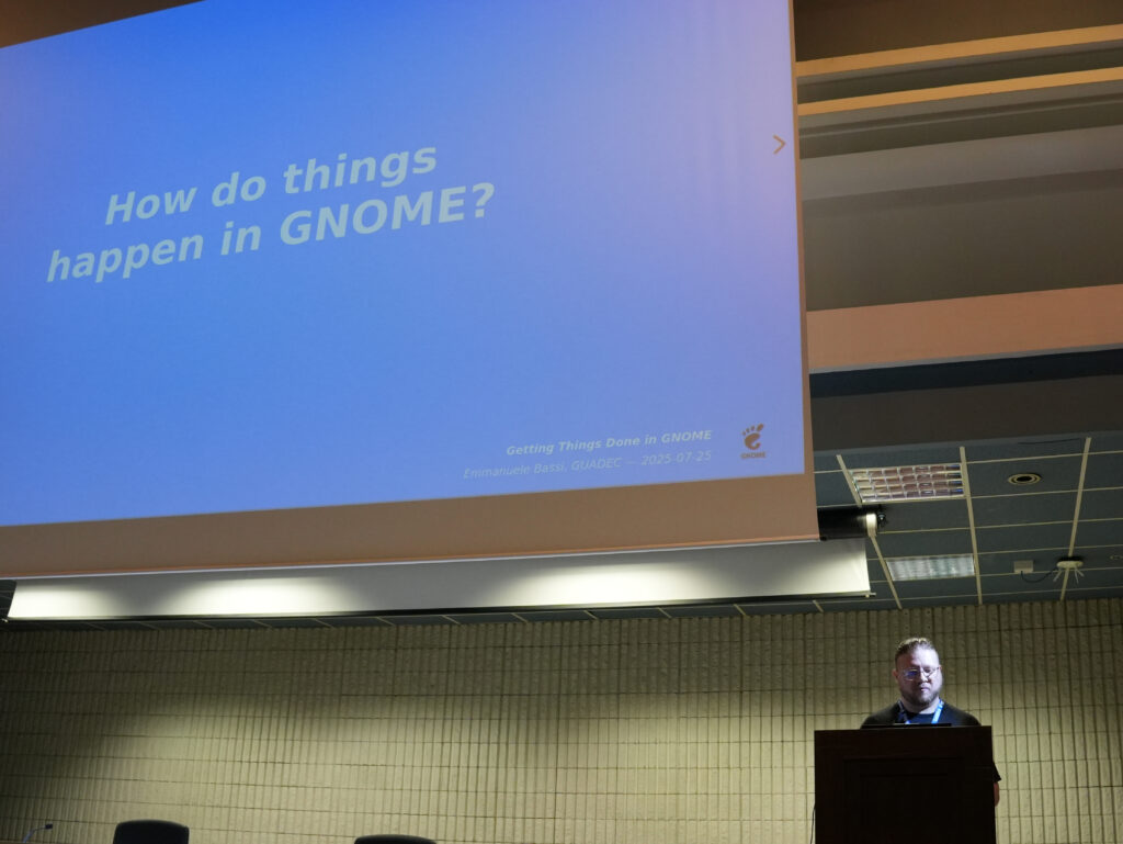 Emmanuele on stage with "How do things happen in GNOME?" on the projector